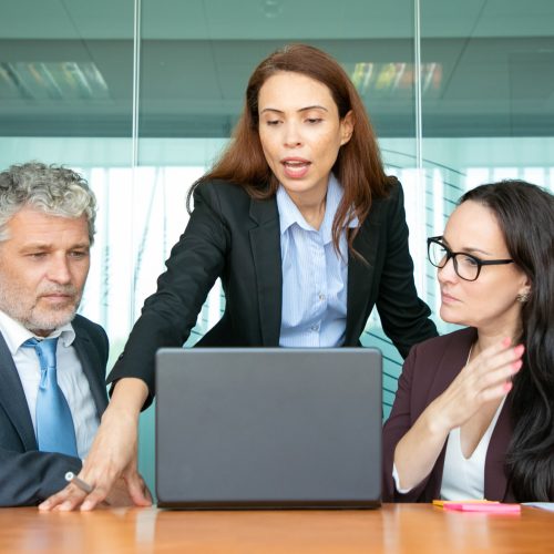 Two women and a man in business suits collaborating and looking at a computer during a meeting.